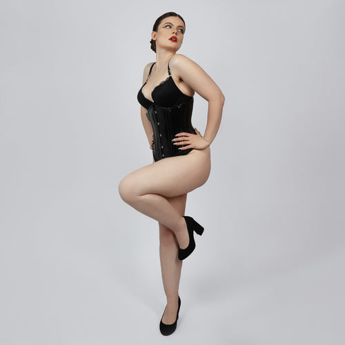 Model wearing black PVC underbust corset from side angle showing hourglass silhouette and hook and eye closure -- Daphne by Corsets Island